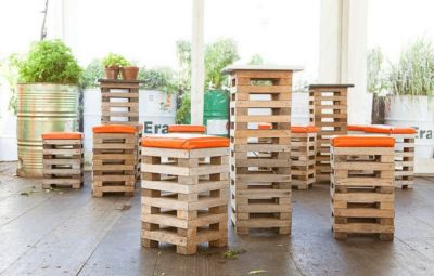 Barkrukken van pallets en hoge tafels van hetzelfde materiaal. Oranje kussens op de zitting.